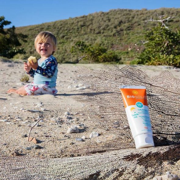 Viser tube med Sun Milk 50 og et lite barn på stranda