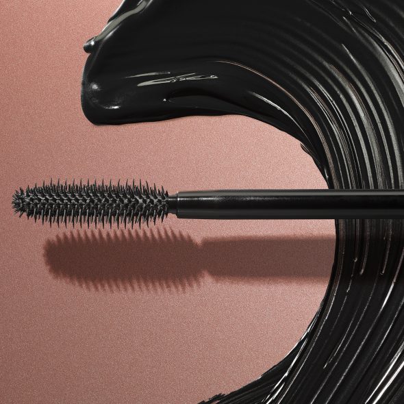 Viser Lash It Loud Mascara børste hode med svart mascara smurt utover i en bølge lignende form på gyllen bakgrunn